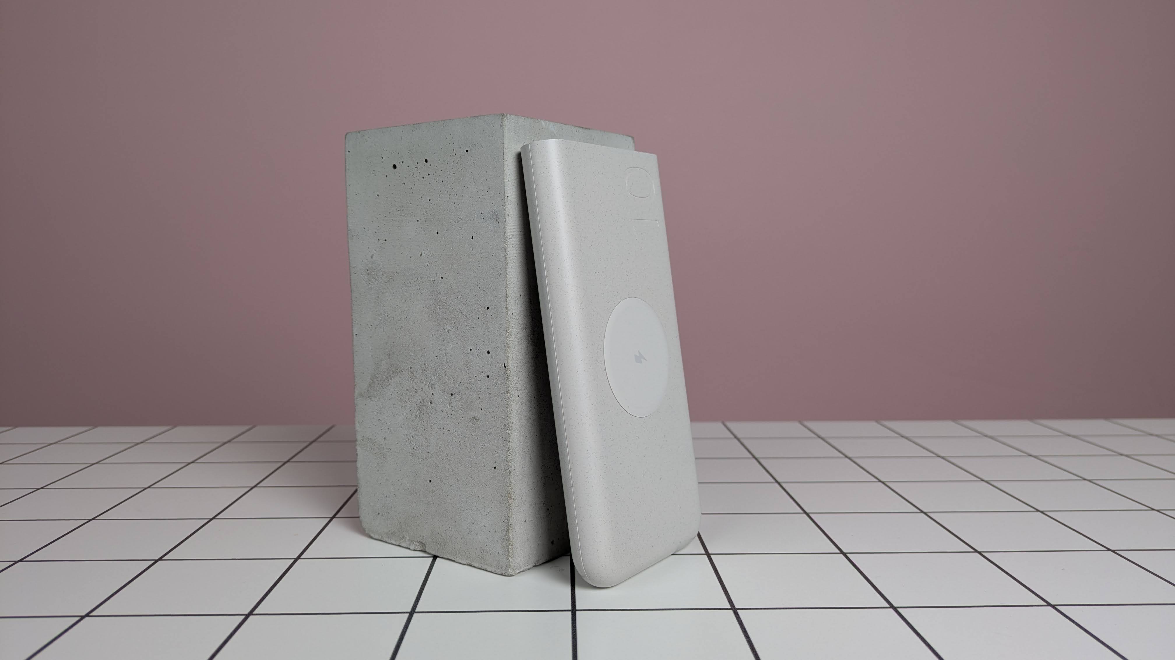 Samsung 25W 10,000mAh Wireless Battery Pack leaning on plinth, on desk with pink background