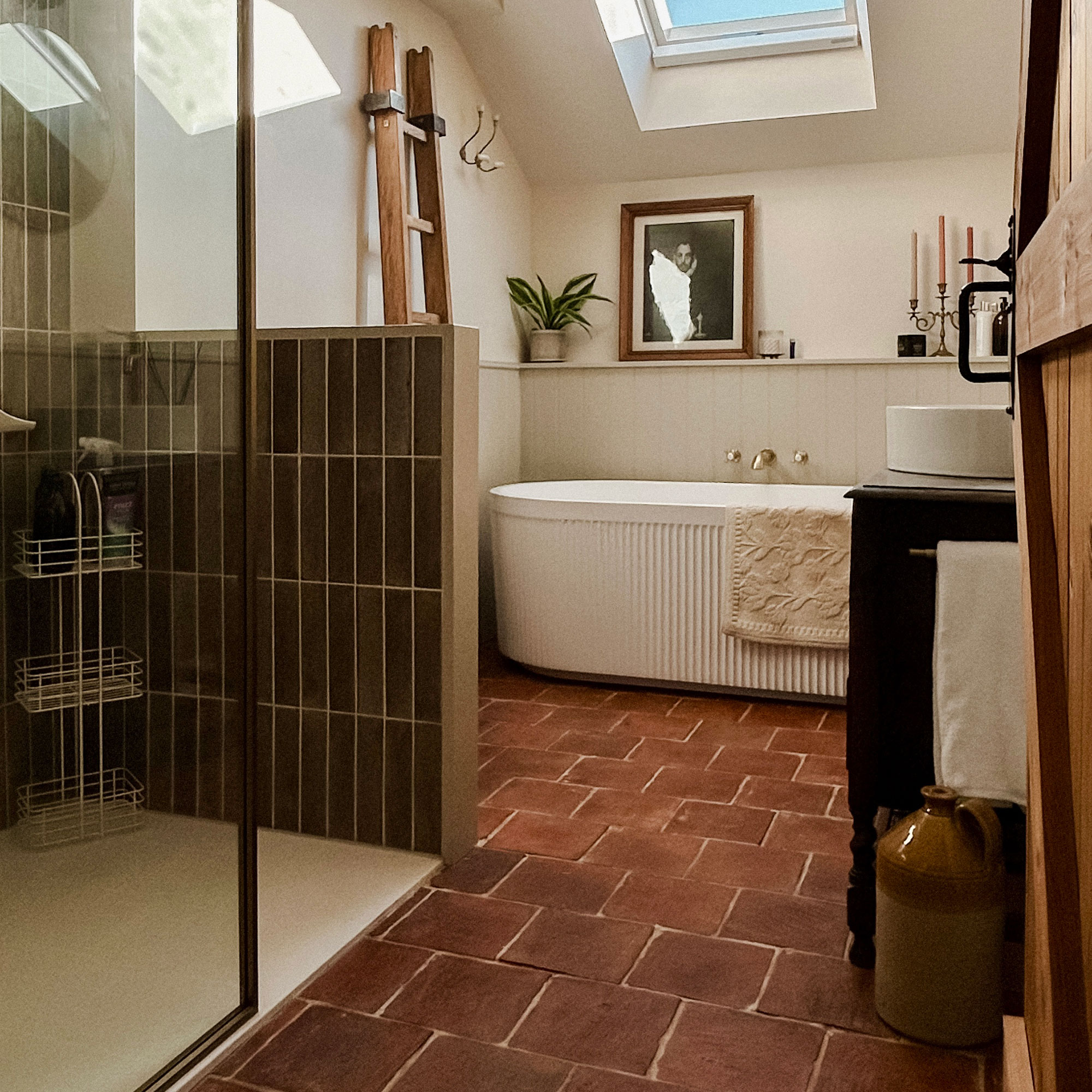 Bathroom with skylight, fluted white bathtub, terracotta floors and shower lined with vertical green tiles