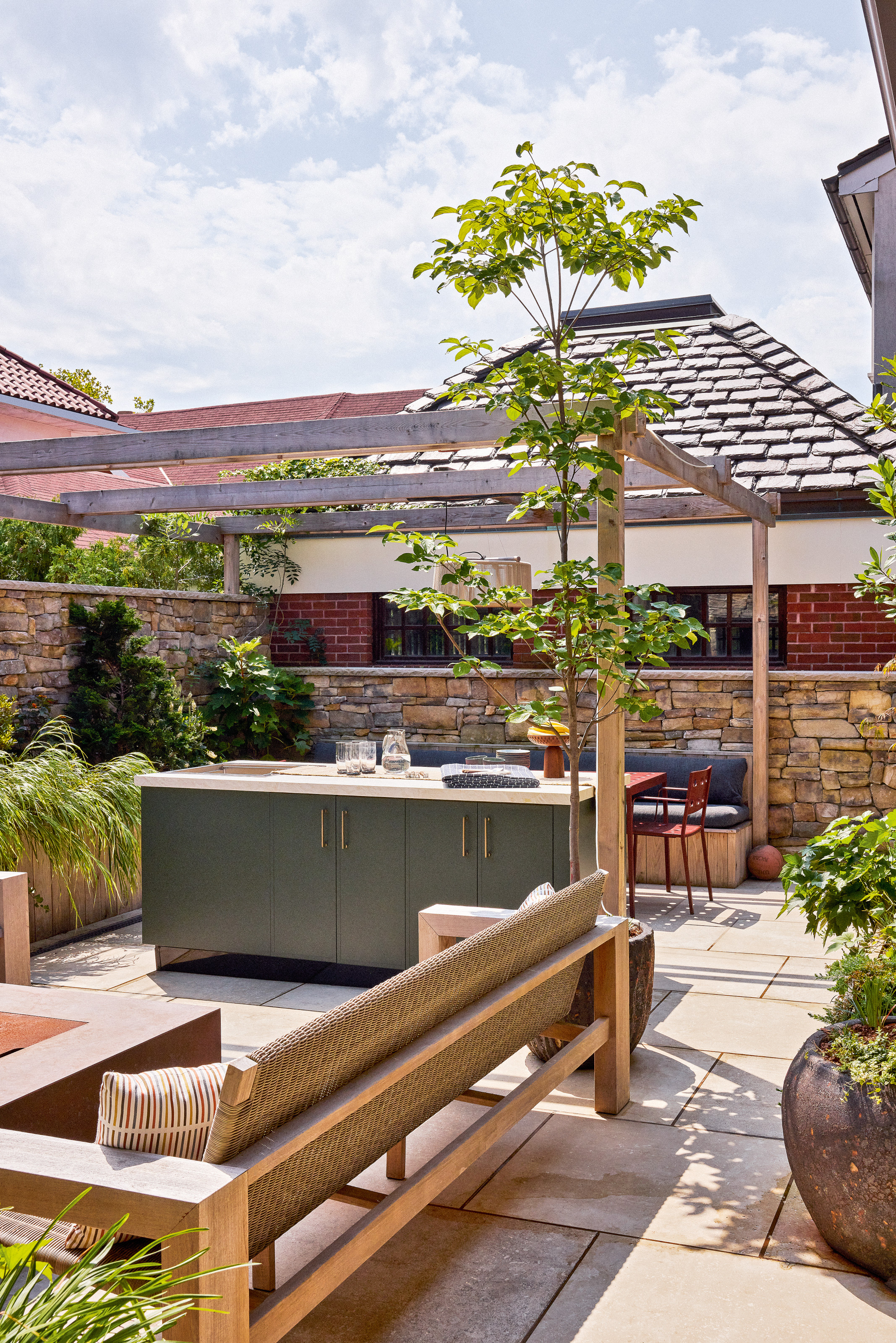 Paved garden with green outdoor kitchen under a pergola, plus bench seating