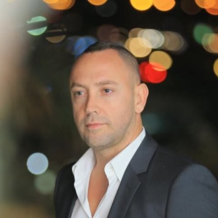 A headshot of Meyr Aviv dressed in smart black suit jacket and white shirt