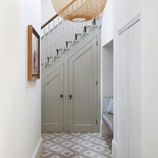 A white narrow hallway wirth a high ceiling and a grey staircase and under-stair storage cupboard at the end of the hallway