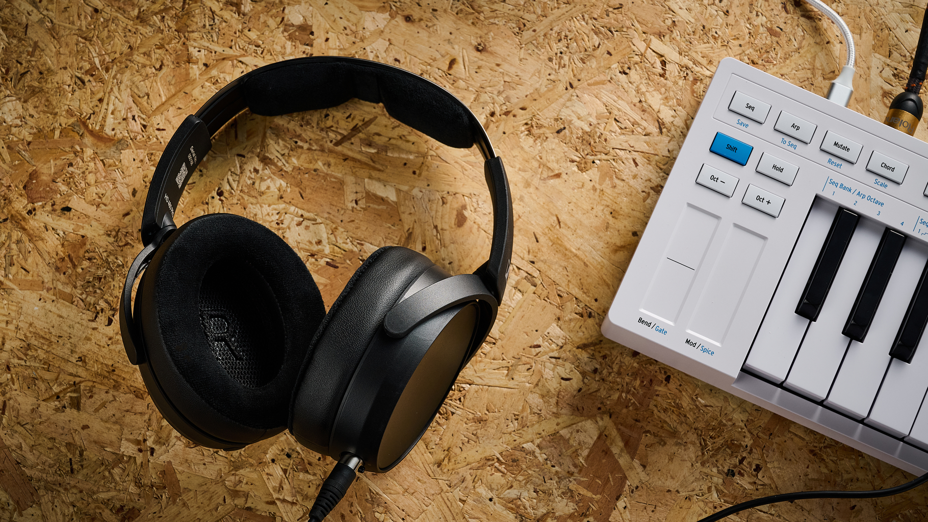 A pair of Sennheiser HD 480 Pro studio headphones lying on a piece of hardwood next to a MIDI keyboard