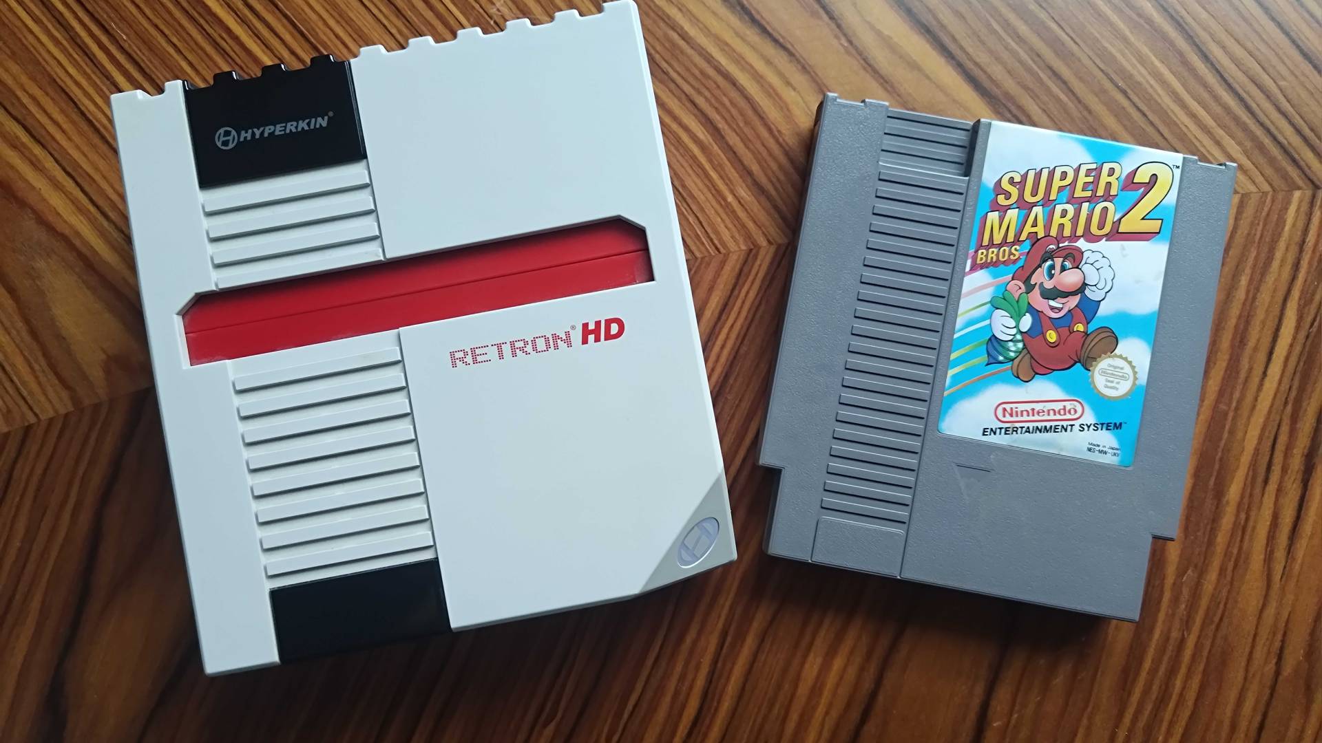 Hyperkin Retron HD on woodgrain table with Super Mario Bros 2 cartridge on right.