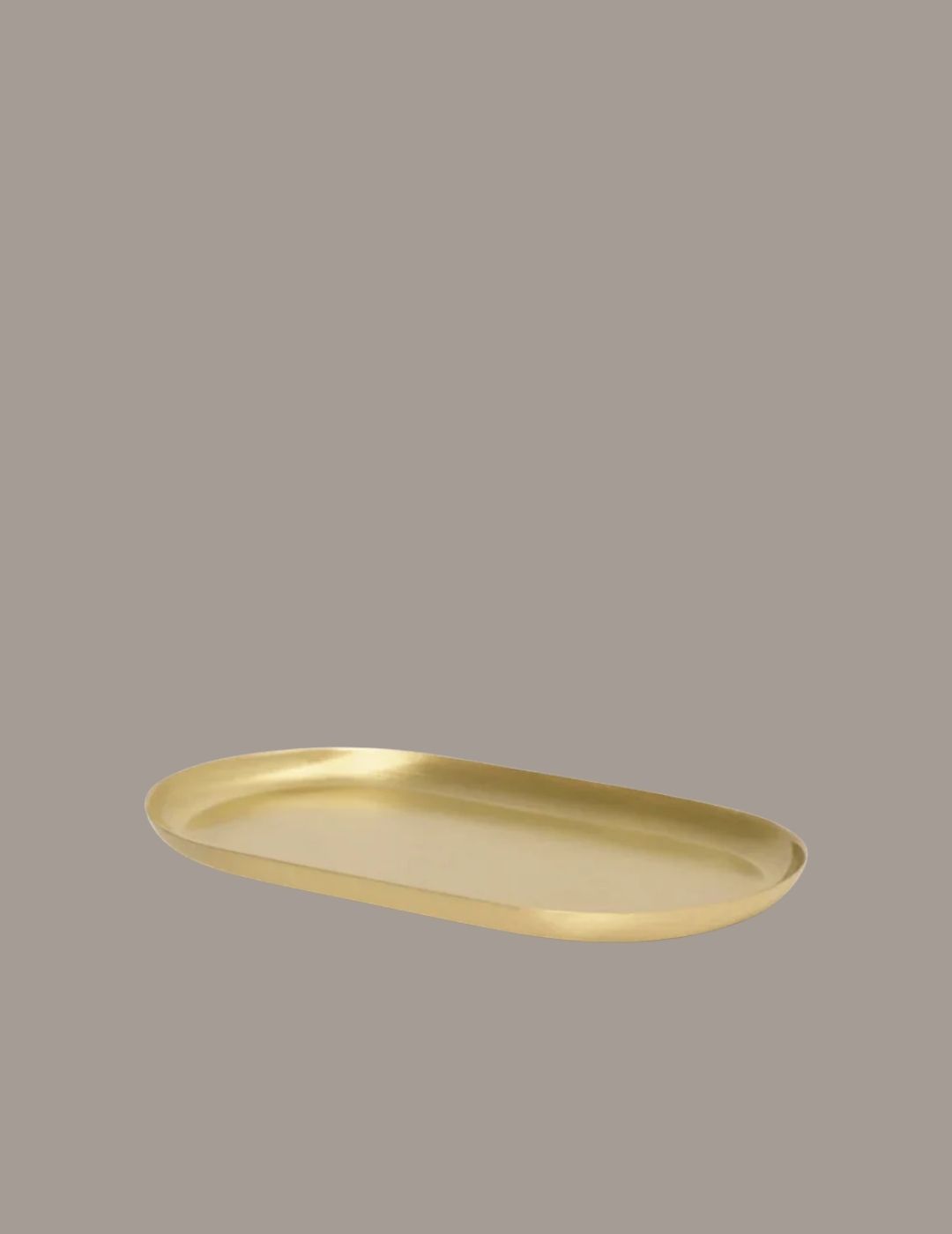 Ferm Living Basho Tray in Oval Brass against brown background.