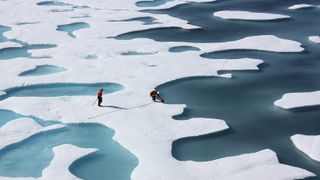 A pair of researchers standing on sea ice surrounded by multiple melt ponds