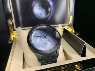 an analog watch with a photo of the moon on its face rests in a case with a beige lining.