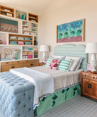 bedroom with neutral wall, green patterned upholstered headboard, shelving unit and blue ottoman
