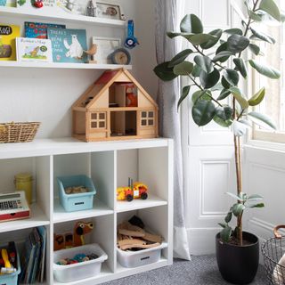 A cubby storage unit used for toy storage in a playroom with floating shelves installed above displaying children's books