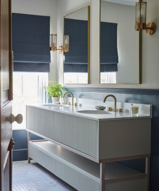 bathroom with mosaic floor tiles, fluted drawer fronts on his and hers washstand, dark blue blind and dark blue wall