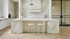 A marble kitchen island with bar stools. The kitchen backsplash also has the same effect on it as the island