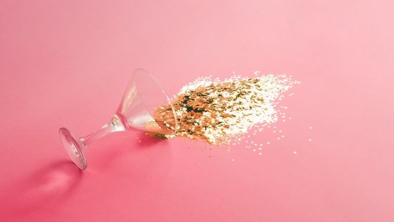 Spilled martini glass full of gold glitter on pink background. Creative minimal party concept. - stock photo