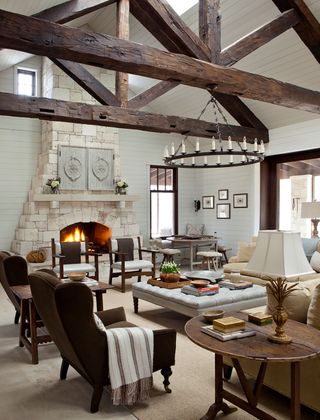 living room with wingback chairs fire lit in stone fireplace chandelier and pale stone floor