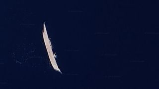 An aerial photo showing a long ship on its side in dark blue water