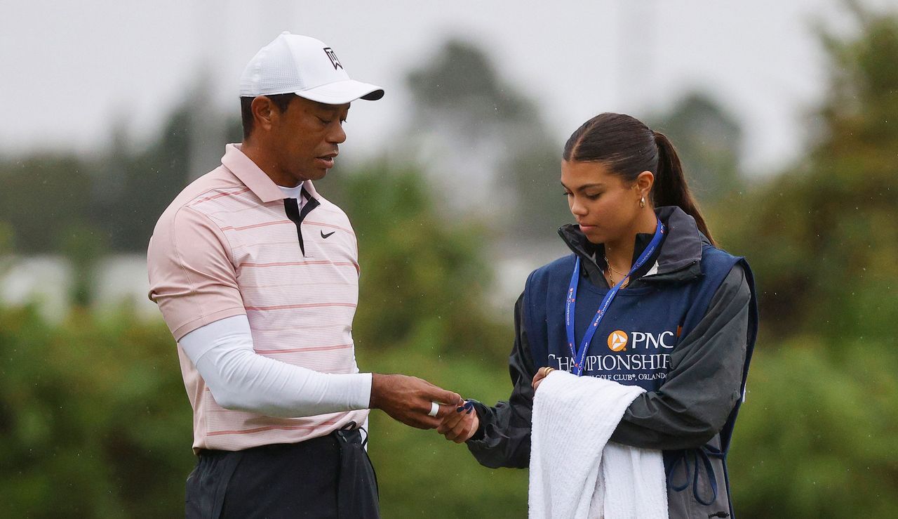 Tiger and Sam Woods chat on the putting green, with Sam holding a towel and Tiger holding a golf ball