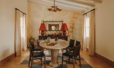Dining room with travertine oval table, wooden chairs, red table lamps and pale beige and orange mural