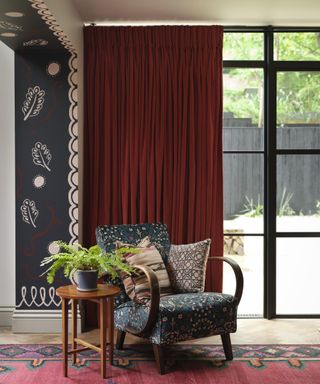 living room with red curtain, patterned armchair, red rug and painted leaf motifs on entryway