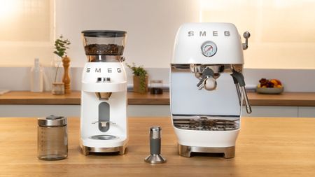 A cream retro manual coffee mahcine beside a matching coffee grinder on a wooden kitchen counter