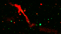 A red ribbon of radio energy blasts out of a black hole on a black background