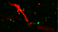 A red ribbon of radio energy blasts out of a black hole on a black background