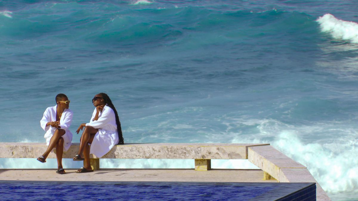 Tolú Ekundare and Winnie Ilesso in white robes by the pool.