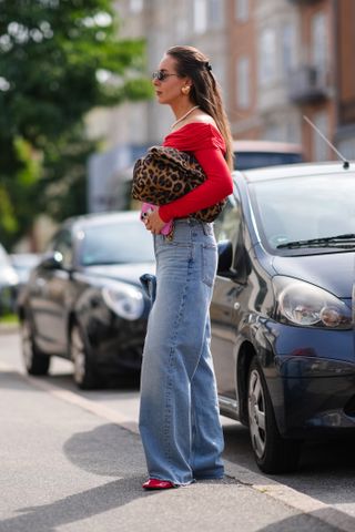 Woman in jeans, red top, and leopard bag.