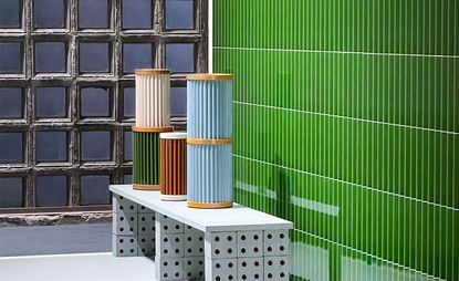 Stacked colourful vases on bench with green tiles in the background