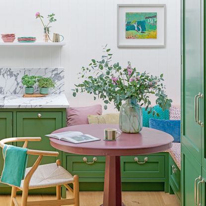 small green kitchen with marble splashback and banquette seating area and painting on wall