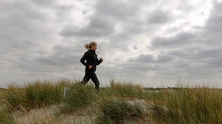 Woman running across sand dunes in workout kit at a low intensity to show 80/20 running