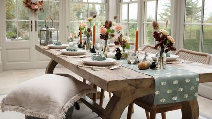 A light wood dining table with a blue runner and blue fabric pumpkins in place settings