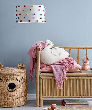 A blue entryway with a wooden bench with a pink blanket, a wicker basket, and a white lampshade