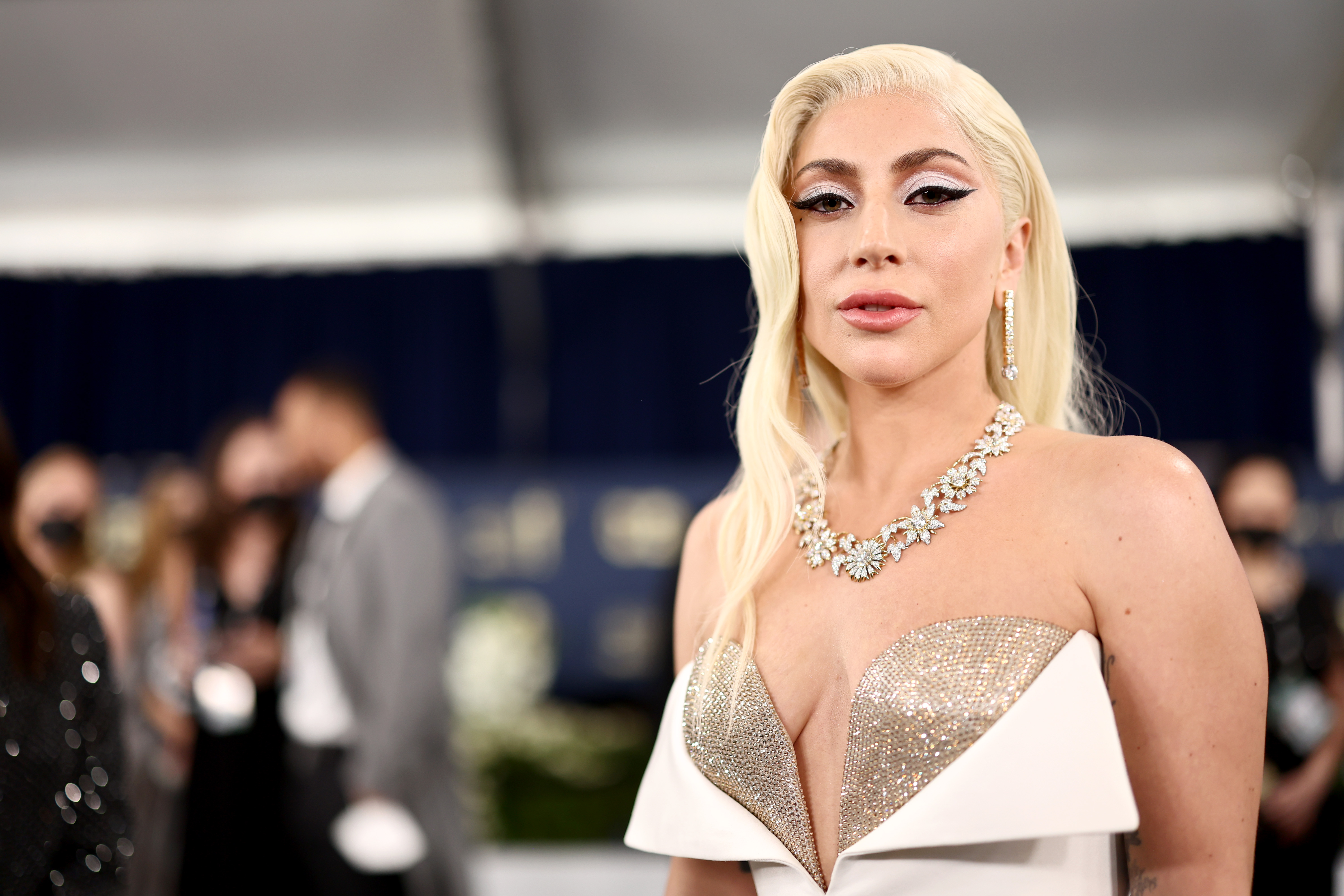 Lady Gaga wears a strapless white and gold dress and has long blonde hair