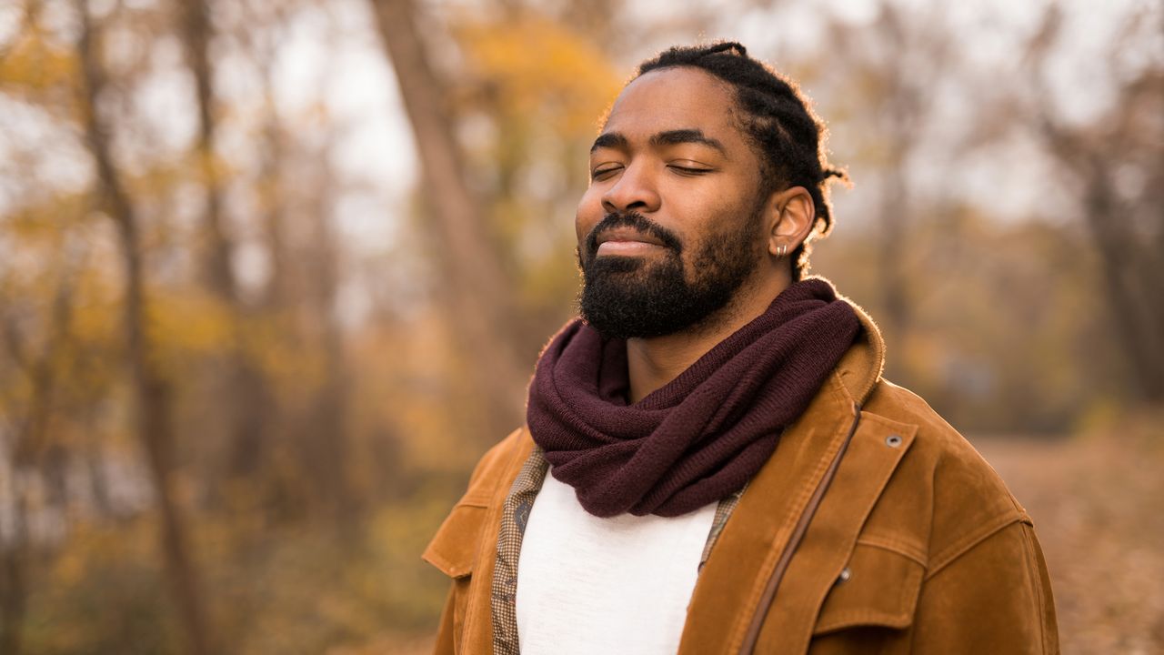 Man in scarf and jacket stood outside looking peaceful and calm with eyes closed