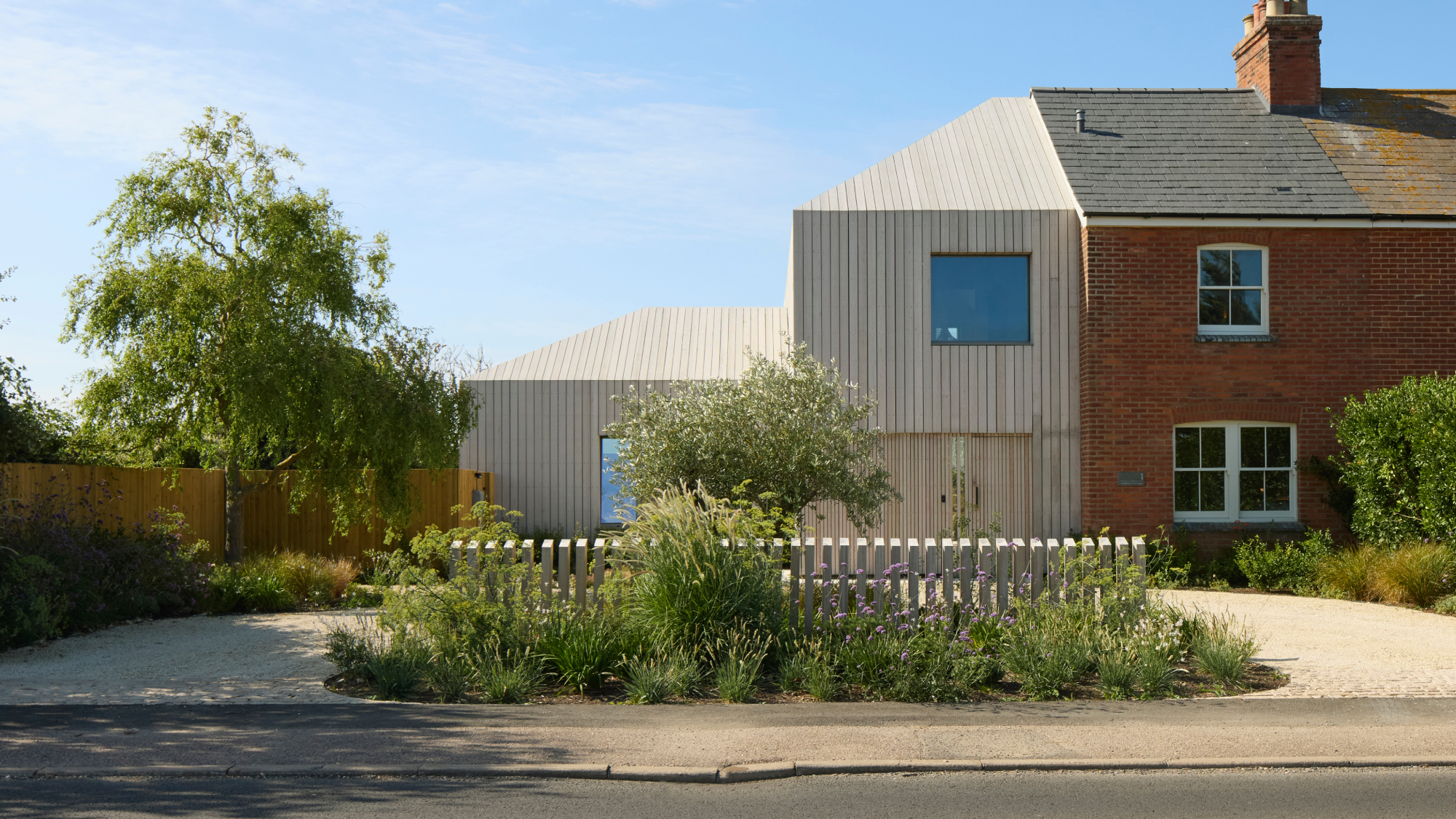 timber clad timber frame extension to large brick property with gravel driveway to front of house