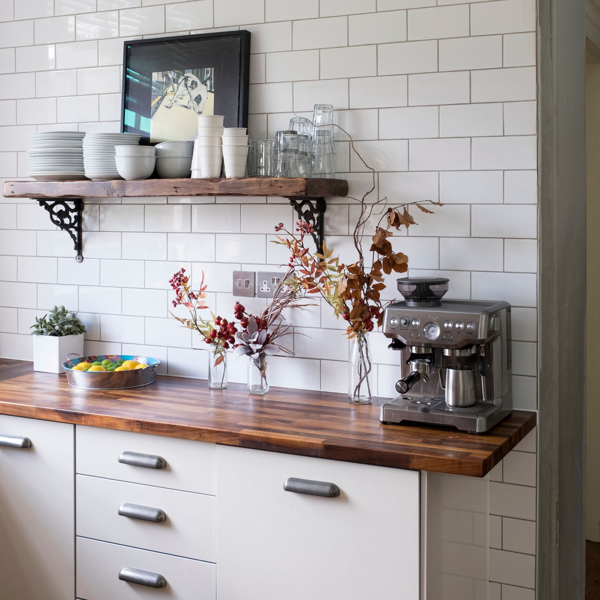 White tiled kitchen with wooden counter and a coffee machine on top of it