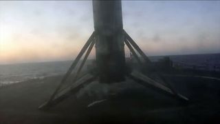 a rocket stage stands vertically on its four landing legs after touching down on an ocean-based drone ship