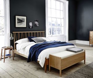 wooden bedroom furniture in bedroom with dark navy walls and white bedding half covered with blue blanket