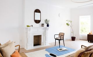 White walled living room with mirror over the fireplace, rug and chairs