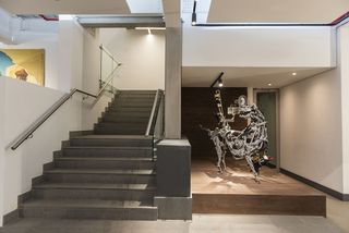 View of the grey staircase at Javett Art Centre and a grey, four-legged mechanical style structure next to it in a space with white walls and spotlights