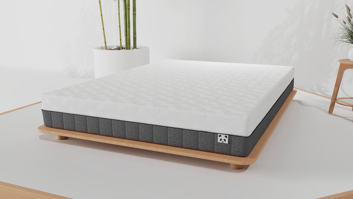 The Panda Hybrid Bamboo mattress on a wooden base in a white bedroom, with a bamboo plant in a white pot behind it and a smaller plant in a white pot on a wooden stool to the side