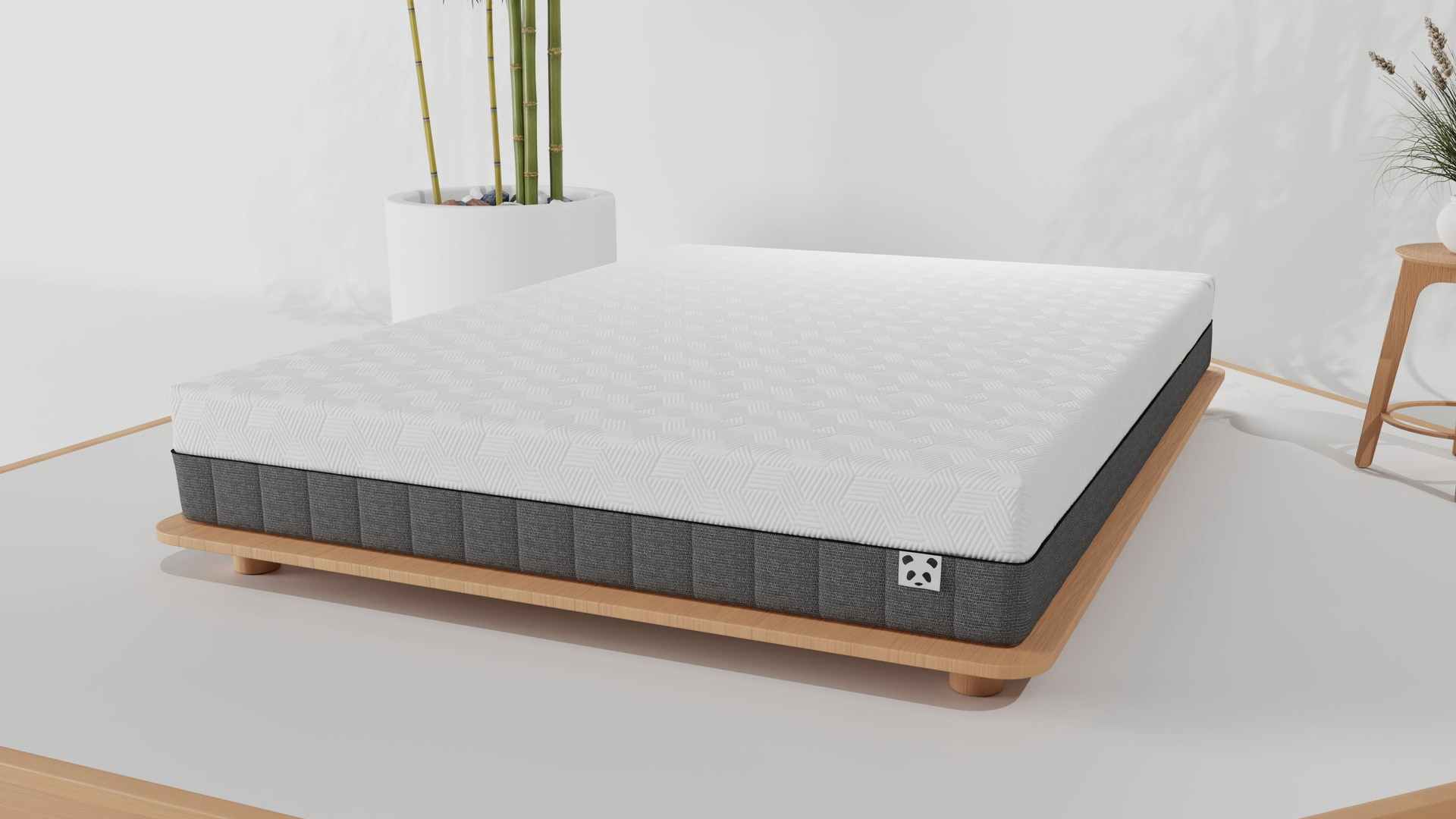 The Panda Hybrid Bamboo mattress on a wooden base in a white bedroom, with a bamboo plant in a white pot behind it and a smaller plant in a white pot on a wooden stool to the side