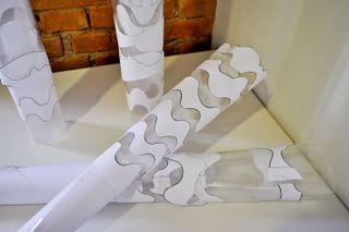 Brick wall left, white wall right, four clear plastic cone shapes with paper design wrapped, emulating the Olympic torch design on a white table top
