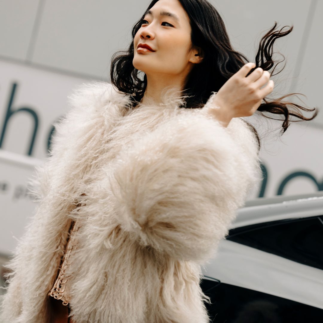 a woman wearing a white fur jacket outside in new york city and flipping her brown hair