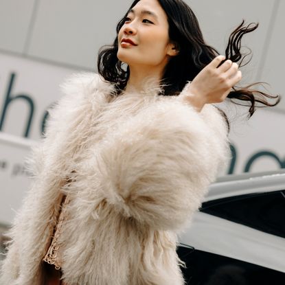 a woman wearing a white fur jacket outside in new york city and flipping her brown hair
