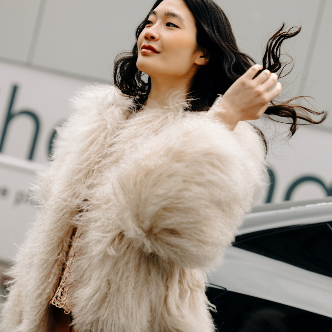 a woman wearing a white fur jacket outside in new york city and flipping her brown hair
