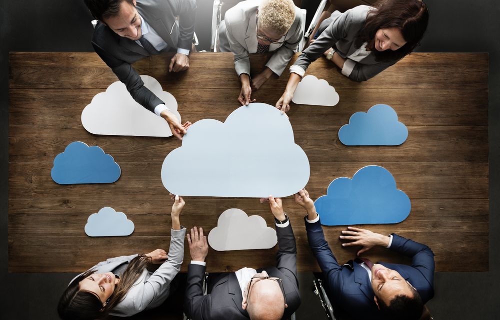 group of people stand around a table with multiple clouds around them