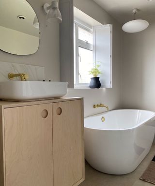 Neutral bathroom with light wood cabinet, marble tiling and window shutters