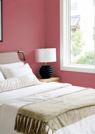 A bedroom with white bedding and earthy pink walls