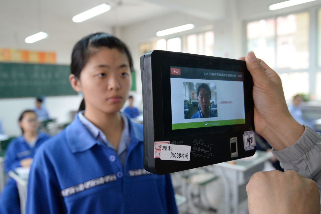 A teacher uses a machine which employs both fingerprint and facial recognition technology to check the identification of a student before a simulated college entrance exam in Handan in China&amp;#039;