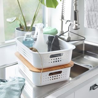 Two stackable baskets with cleaning products next to sink