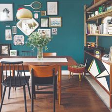 A teal-painted dining room with a table and mismatched chairs